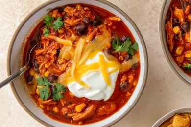 A bowl of chicken enchilada chili topped with sour cream shredded cheese beans and cilantro