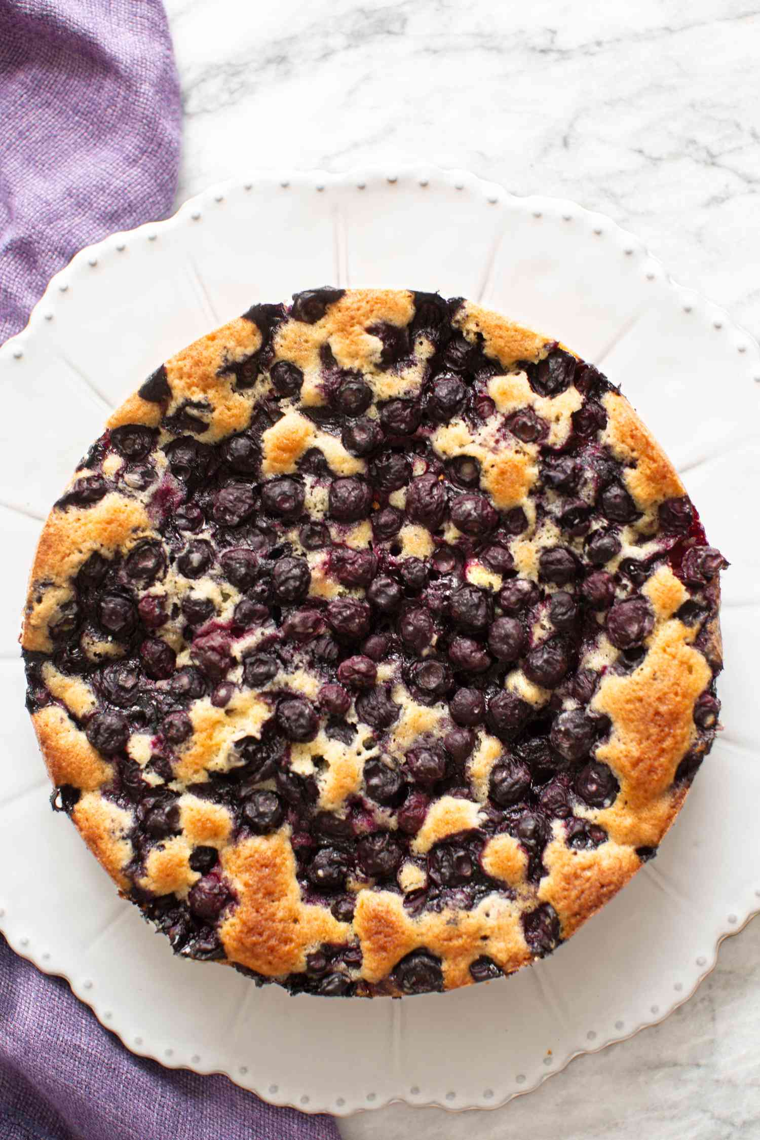 Blueberry Cake on a Plate Next to a Purple Kitchen Linen