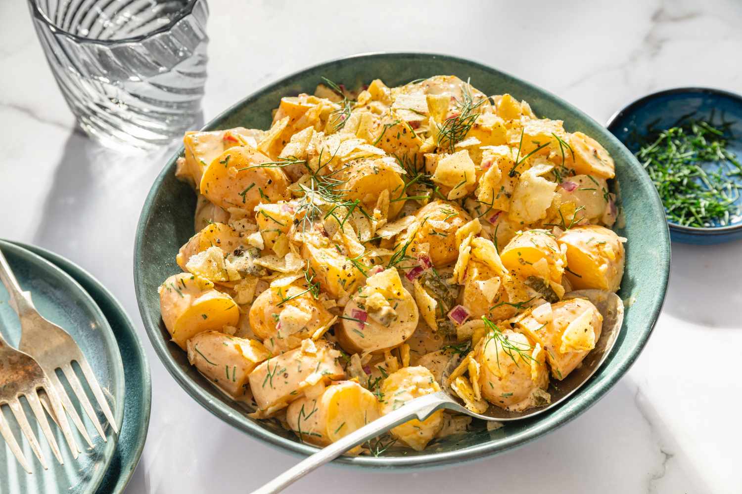 A dish of potato salad garnished with dill on a table