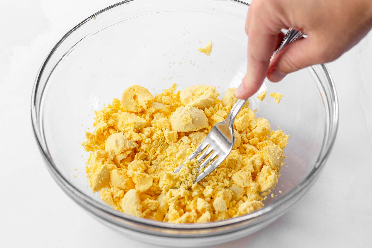 Hard boiled egg yolks mashed with a fork in a glass bowl.