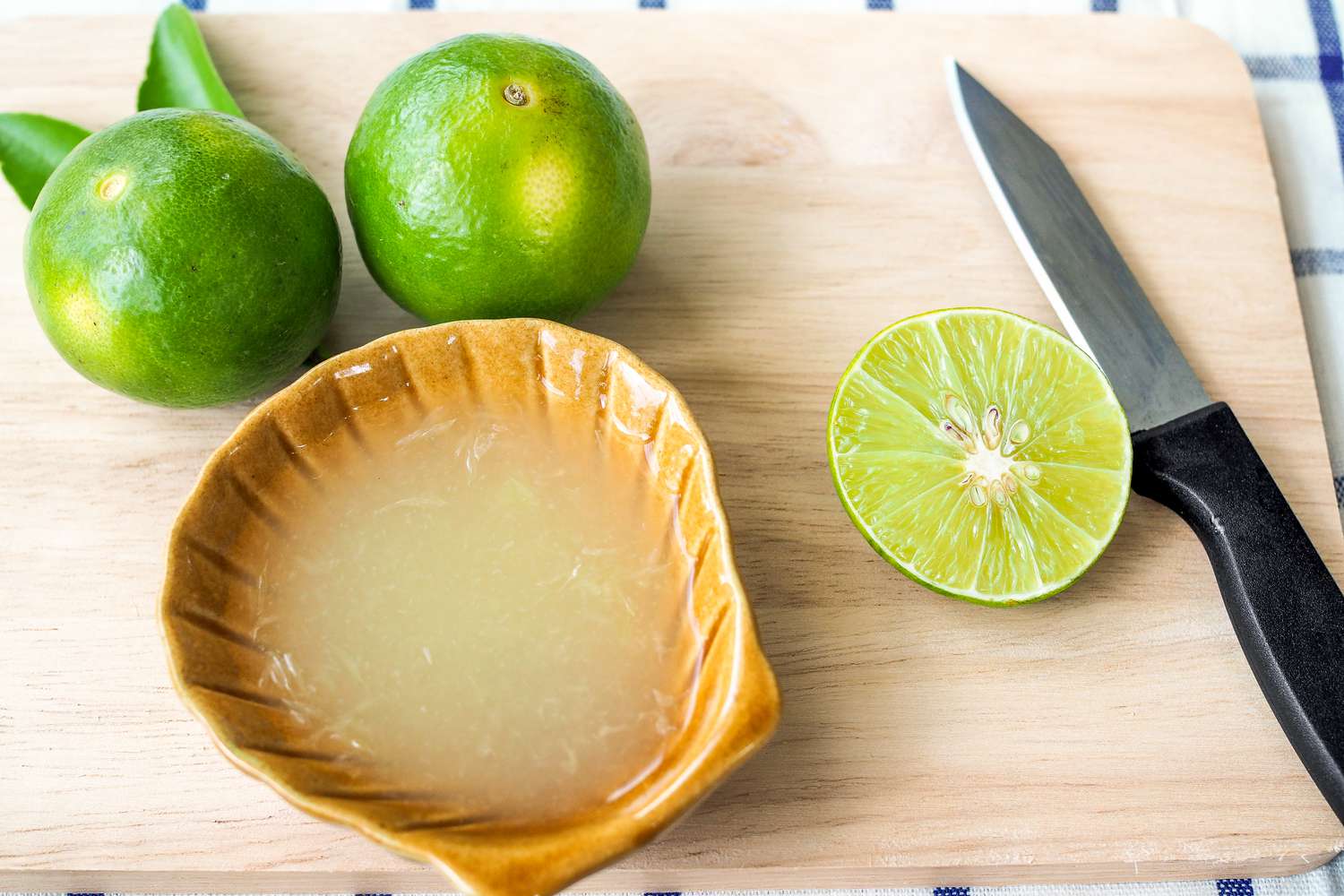 Juiced and whole limes on a cutting board with a knife