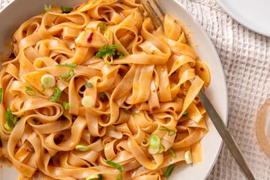 Overhead closeup shot of a serving plate with broad rice noodles in a garlic sauce, garnished with sliced scallions