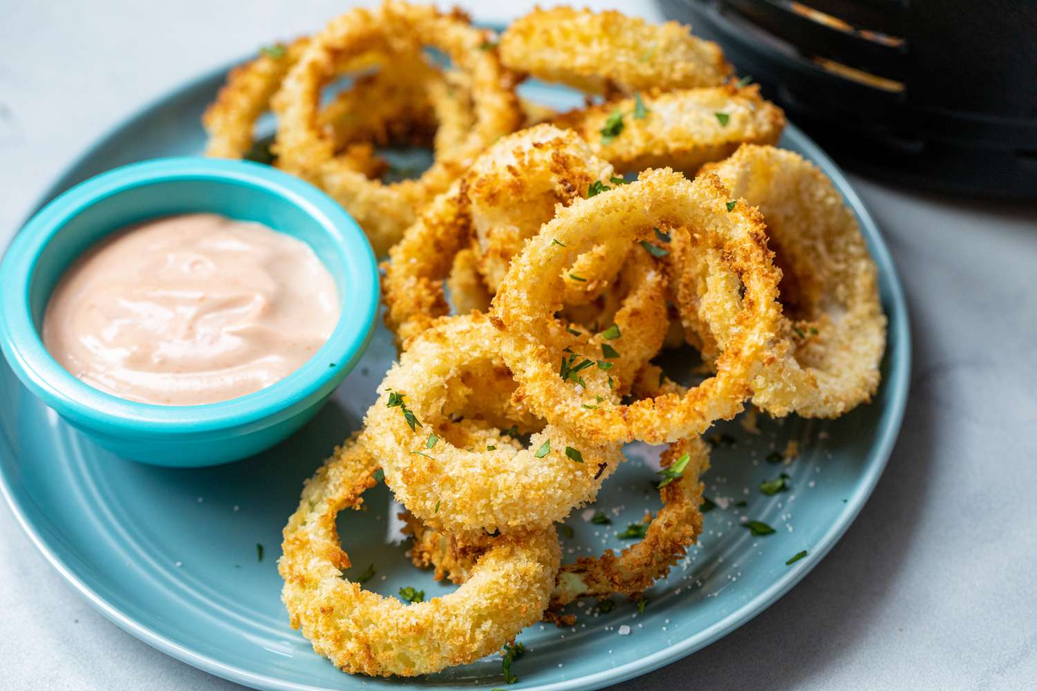 Crispy Air Fryer Onion Rings stacked on a plate with a dipping sauce.