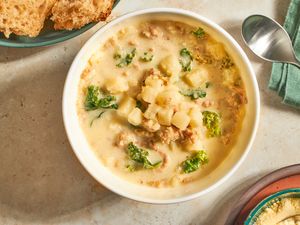 A bowl of sausage kale and potato soup served with bread and grated cheese