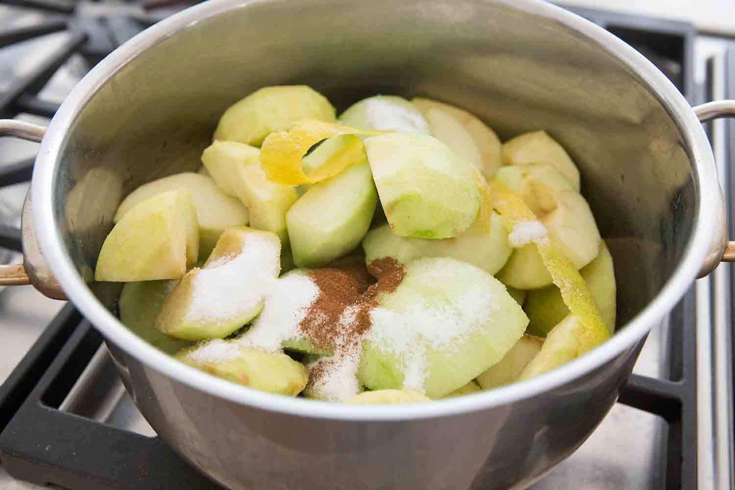 A pot with peeled apples, lemon zest, spices, and sugar before cooking in a pot