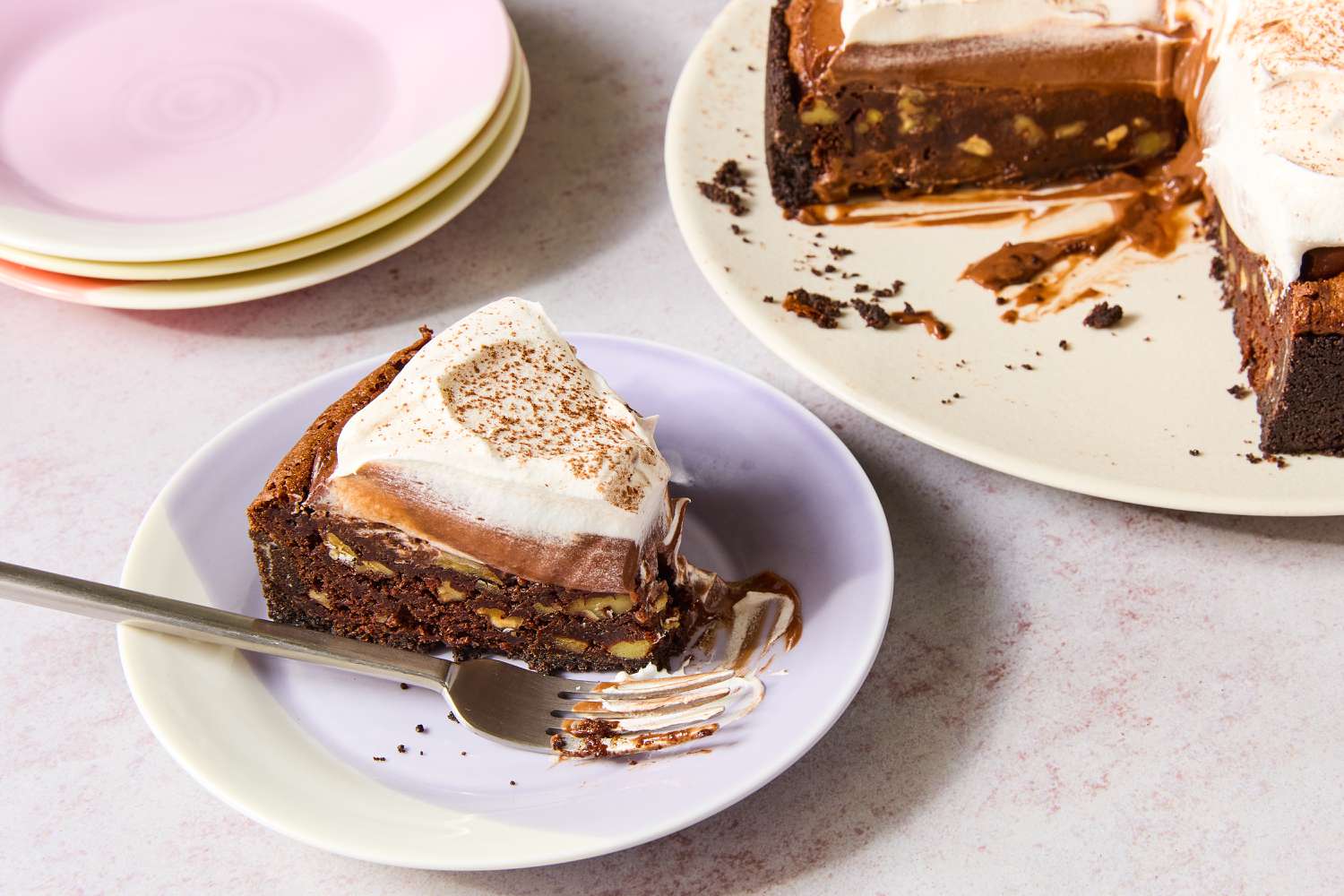 Image of a small multicolored plate with a slice of Mississippi Mud Pie with a fork next to a plate of the pie with several slices removed and a stack of empty plates