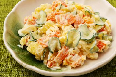 A bowl of potato salad with cucumbers and carrots on a green plate