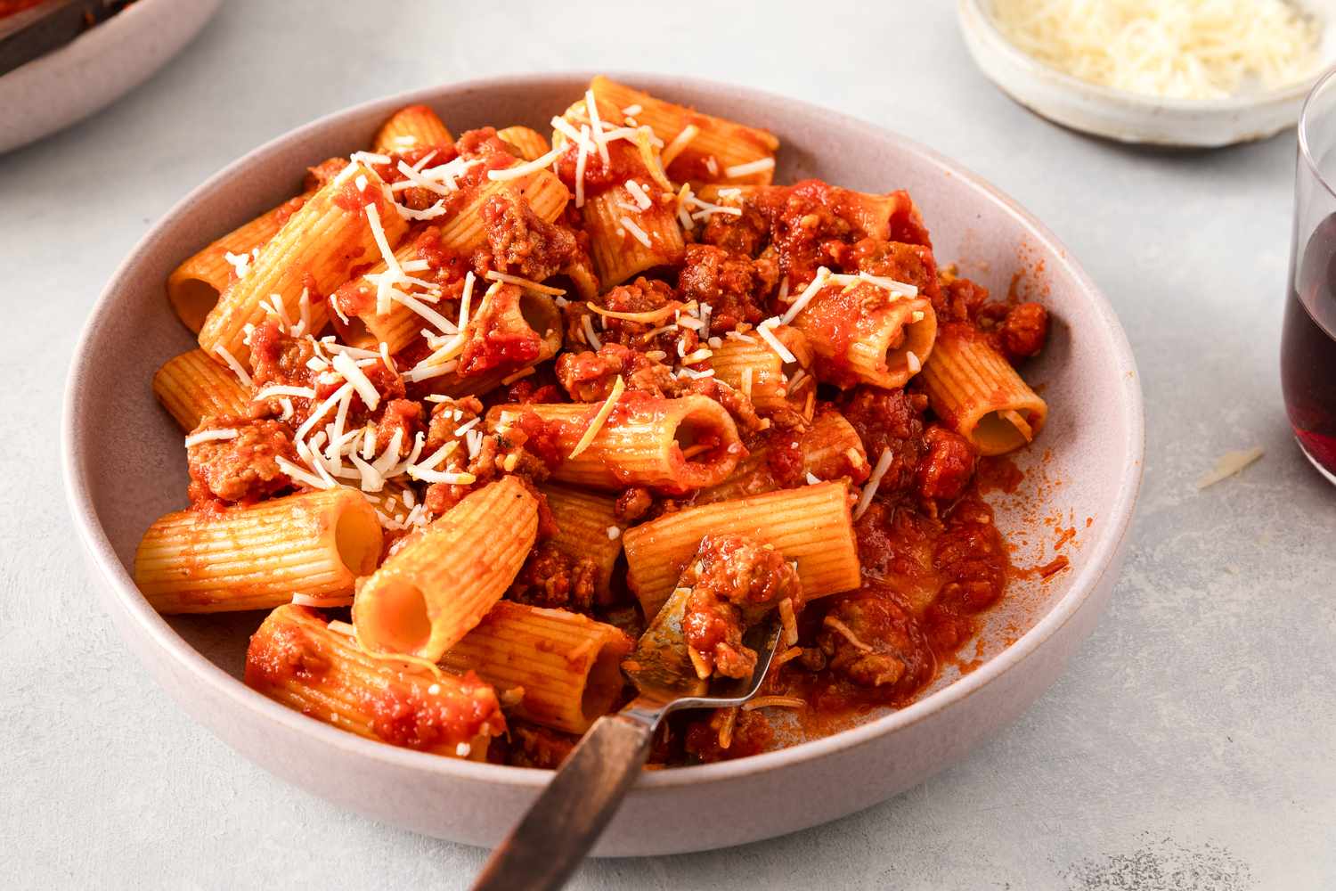 A bowl of pasta with sausage and tomato sauce topped with grated cheese served with a fork