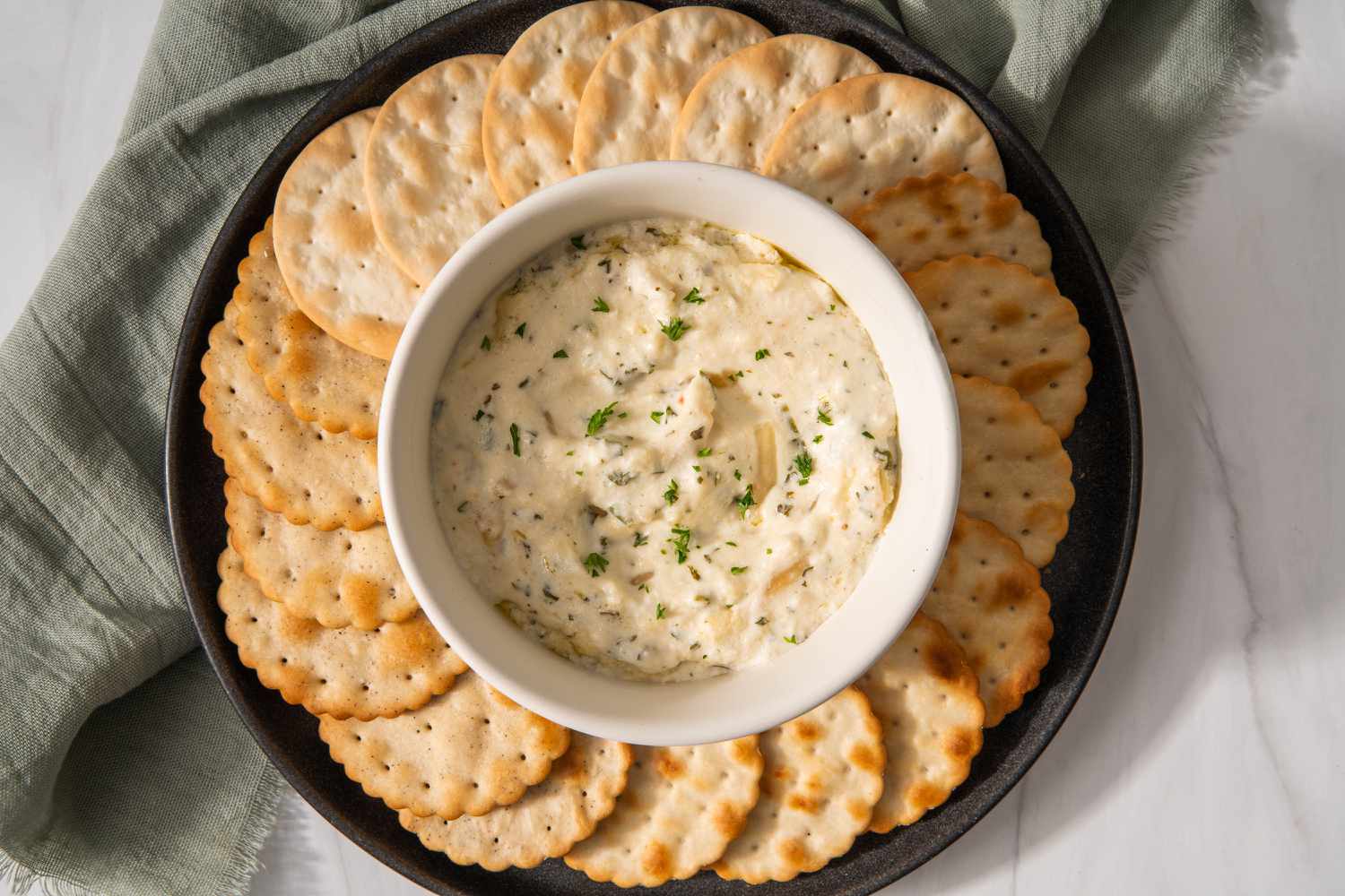 Overhead view of a platter of round crackers around a small bowl of hot crab dip