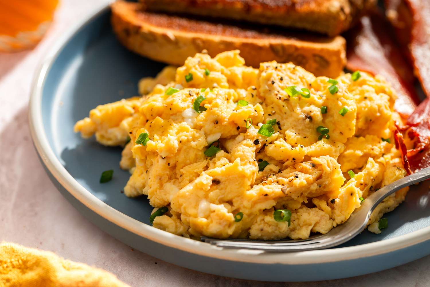 Scrambled eggs topped with chives on a plate next to toast and bacon