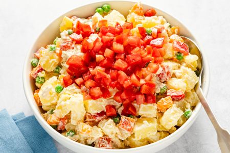 A bowl of potato salad with diced tomato garnish on top containing peas carrots and creamy dressing