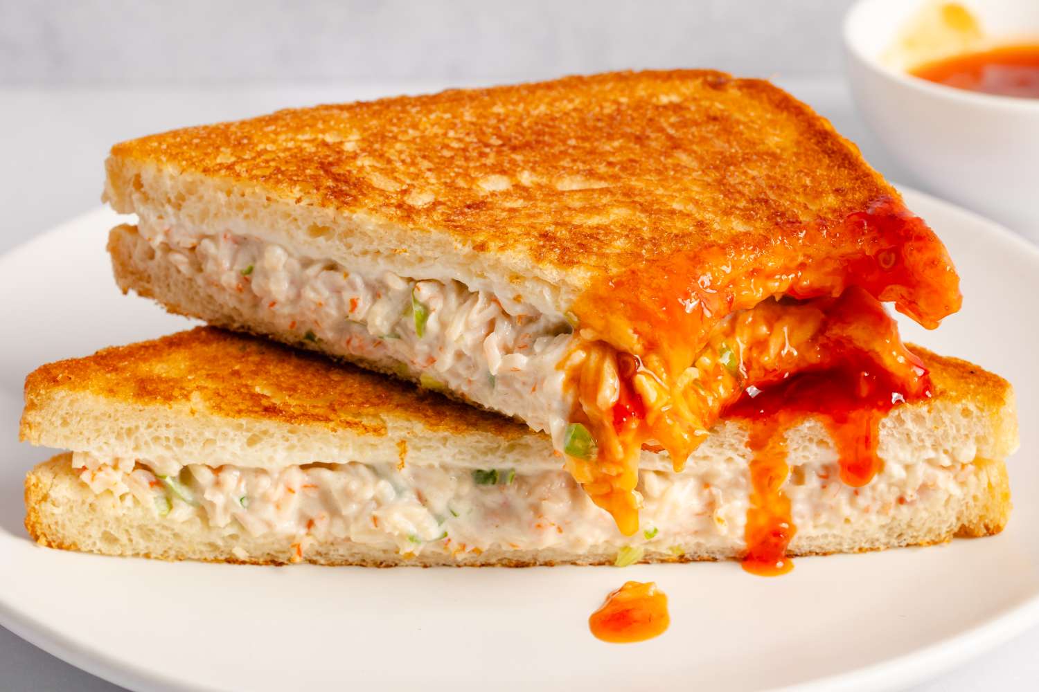 Grilled sandwich filled with a creamy crab mixture served on a white plate with a sweet and sour dipping sauce