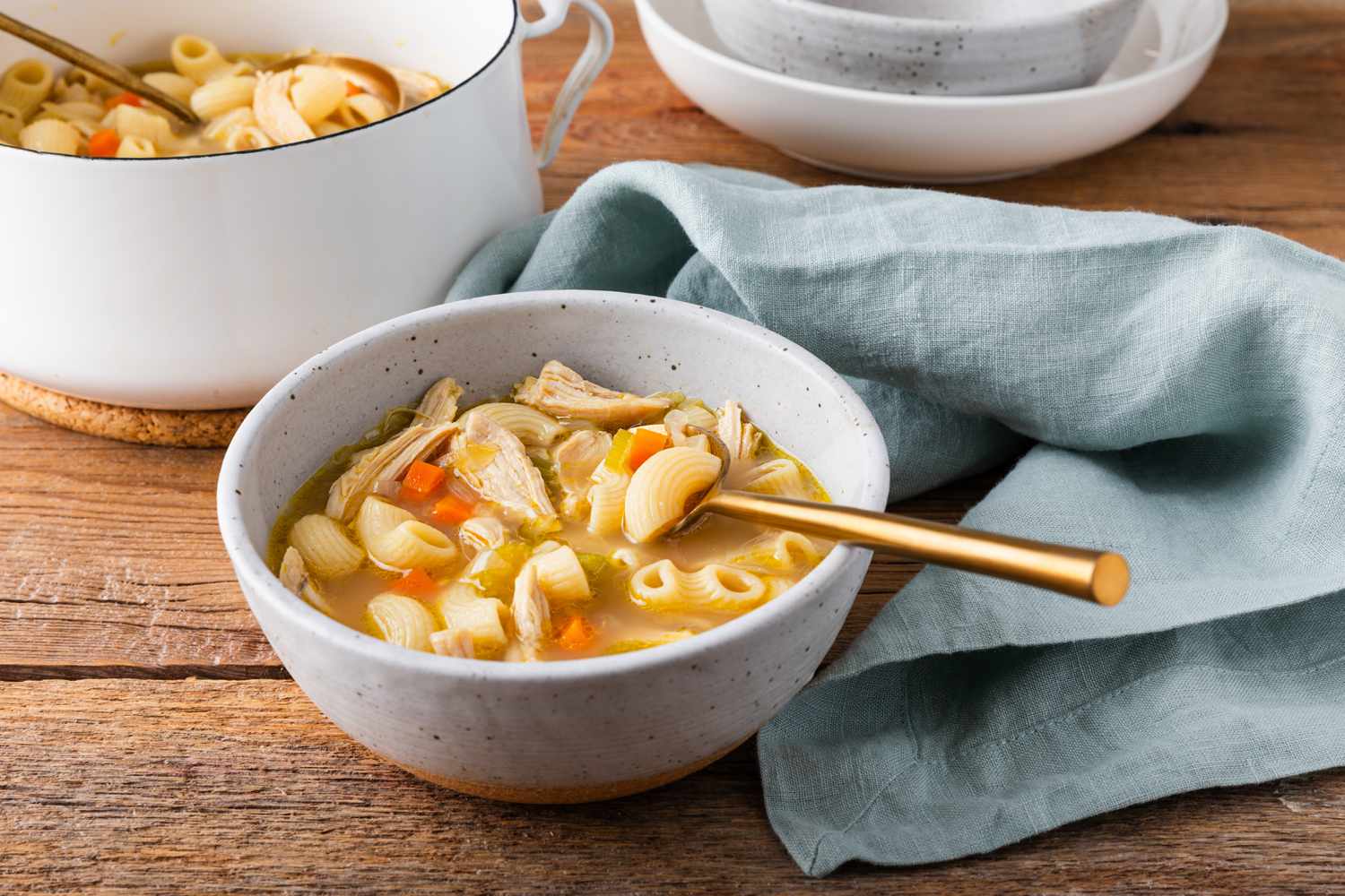 A bowl with a serving of macaroni chicken sopas (Filipino chicken noodle soup), with a pot of soup in the background