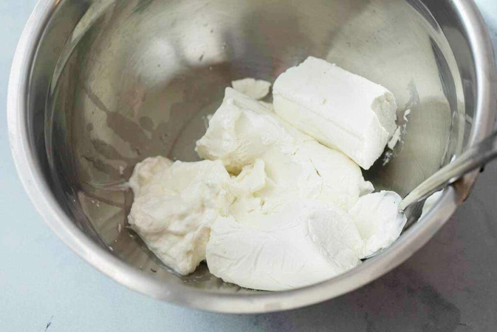 Whip goat cheese in a stainless steel bowl for 7-layer dip