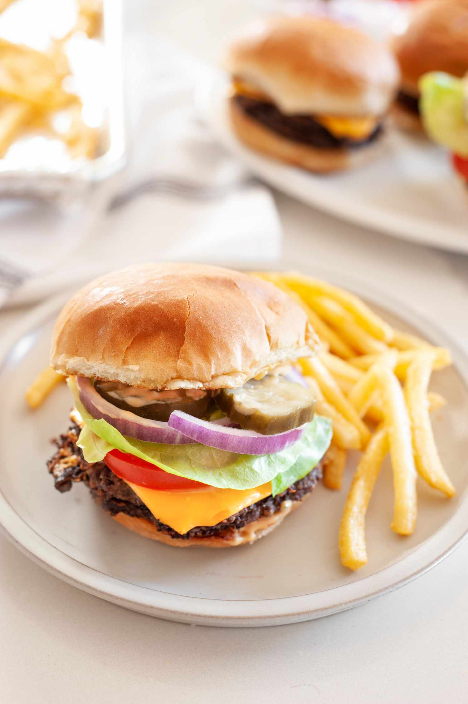 Black Bean Smash Burger on a Plate with French Fries, and in the Background, a Plate with More Burgers and a Tray with More Fries