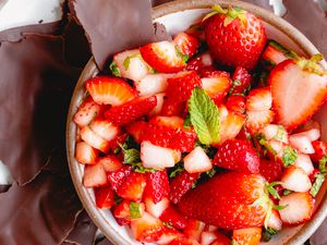 A bowl of strawberry salsa surrounded by chocolate pieces
