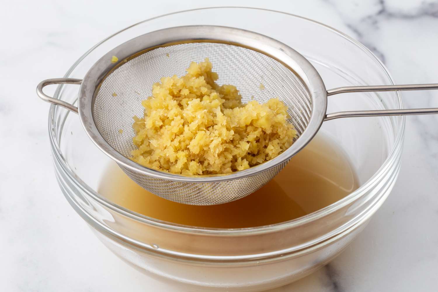 Straining fresh ginger in a glass bowl to make a ginger drink.