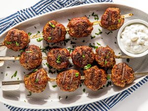 Platter of Grilled Meatballs With a Small Bowl of Tzatziki, All on a Blue and White Stripped Kitchen Towel