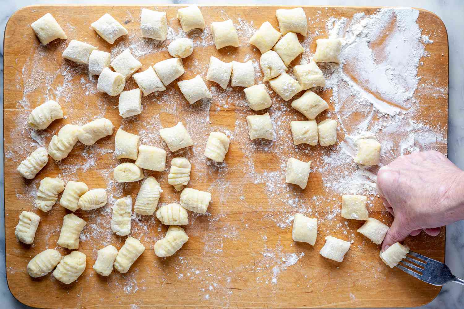 Hands putting dimples in cut Potato Gnocchi and shaping them with a fork