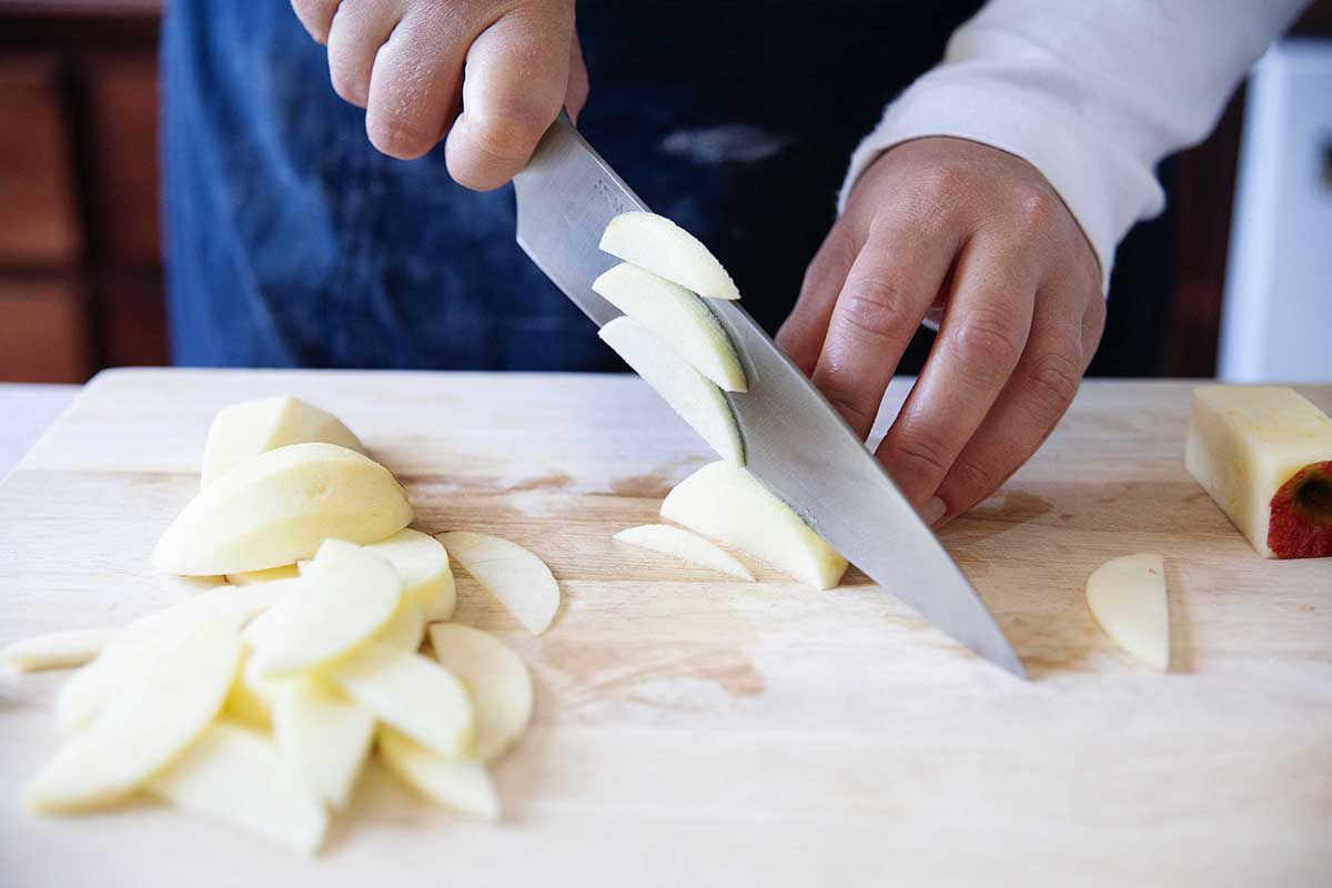 Woman in blue apron thinly slicing apples.