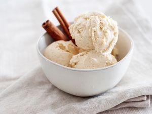 A bowl of cinnamon ice cream with two cinnamon sticks in the bowl.