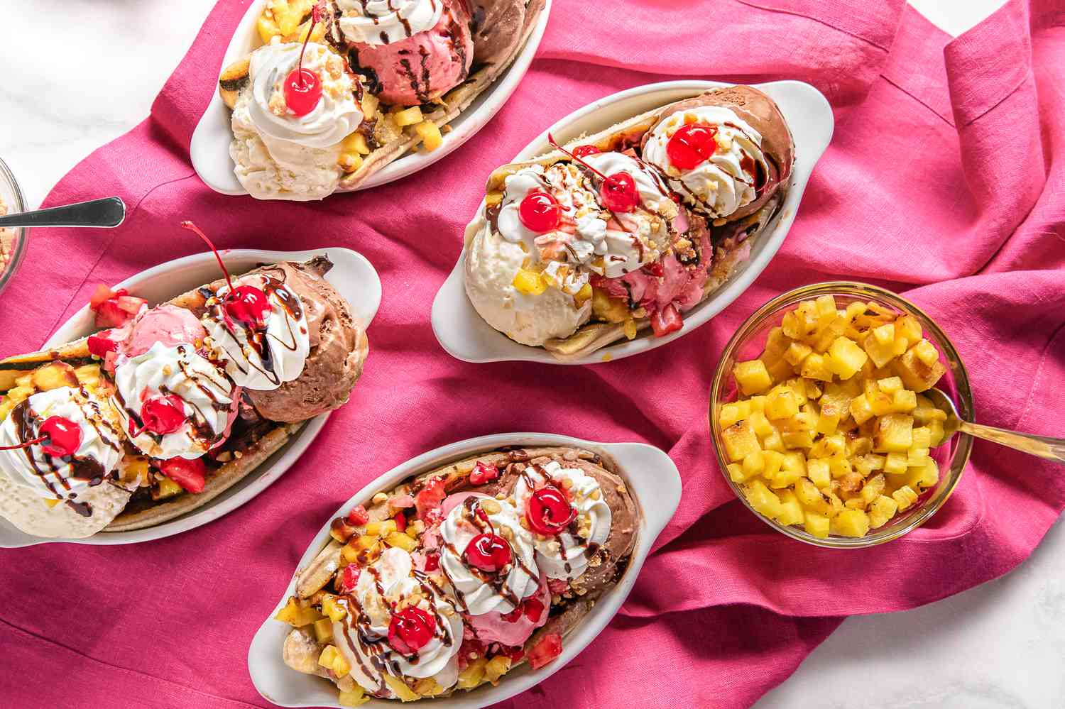 Four Grilled Banana Splits Topped With Chocolate Sauce, Peanuts, Whipped Cream, and Three Maraschino Cherries in Banana Split Dishes and a Bowl of Diced Pineapples