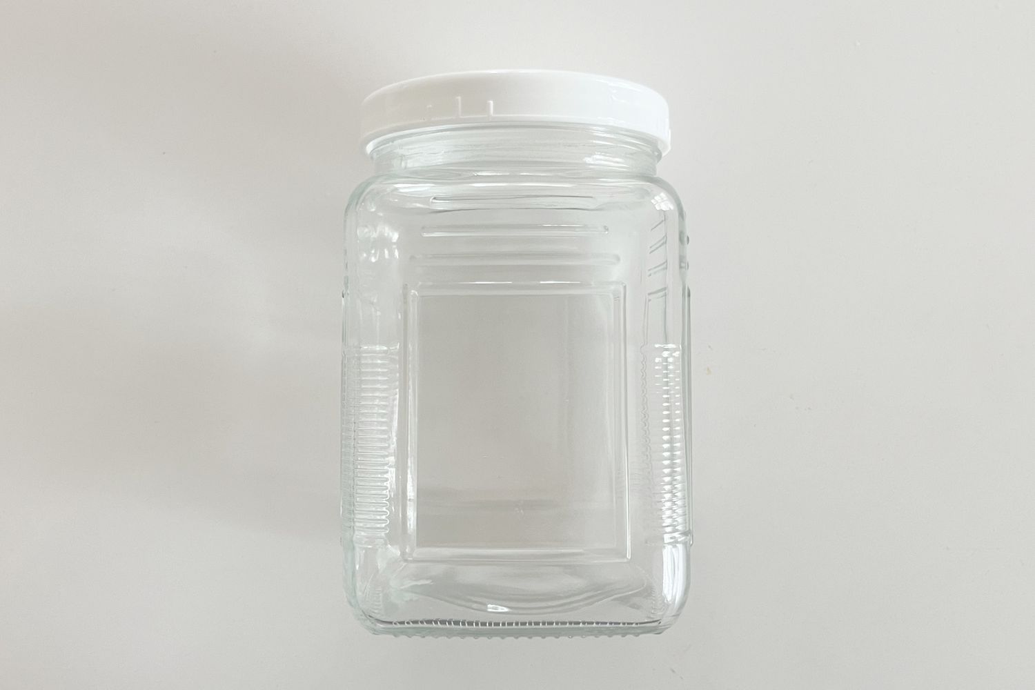 A square glass jar with a white lid on a plain background