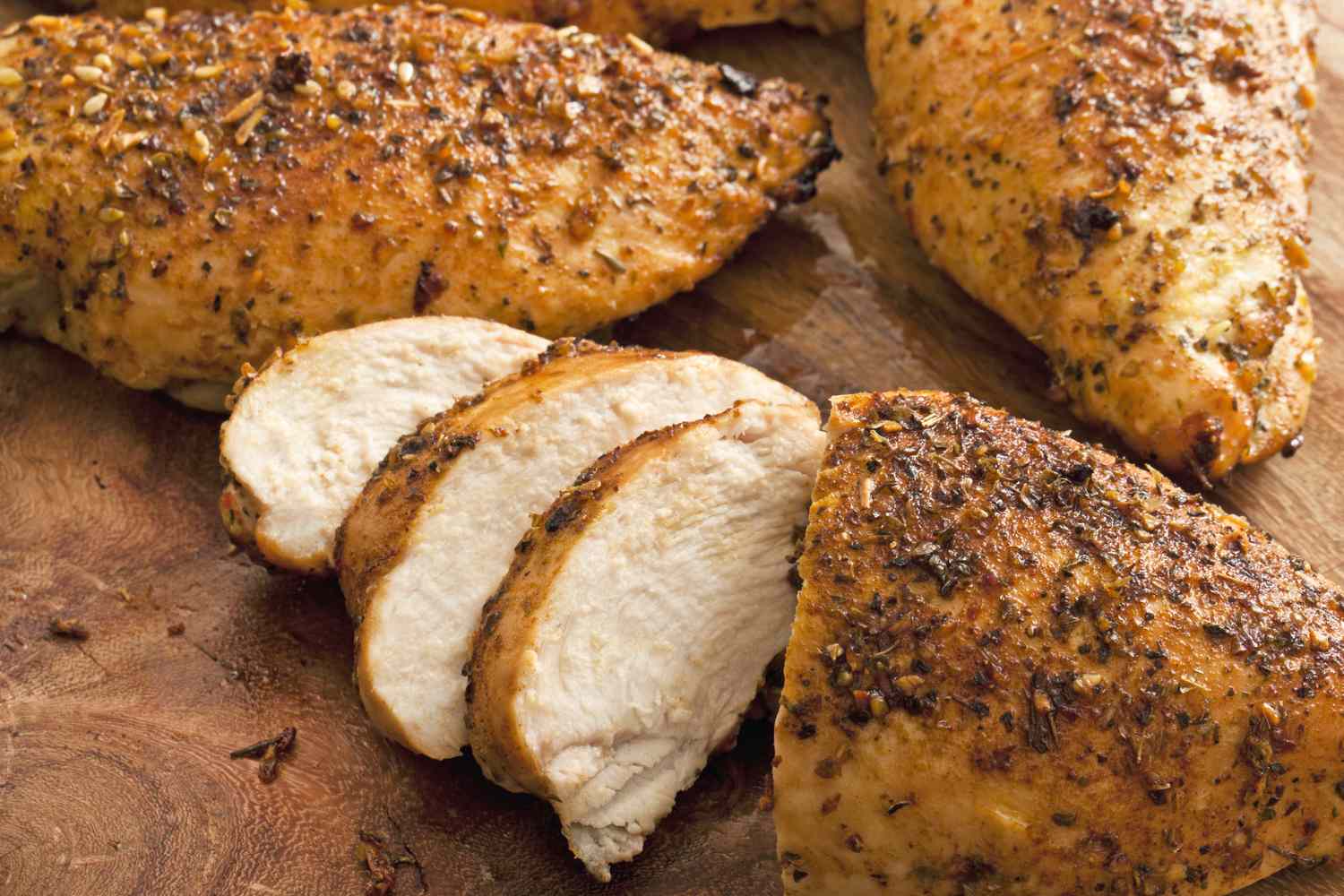 Cooked chicken breasts seasoned and sliced on a wooden surface