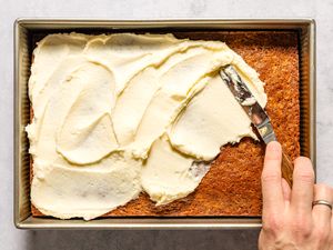 A hand spreading frosting on a rectangular cake with a spatula