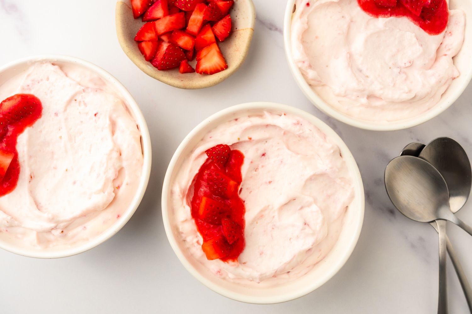 Strawberry mousse in bowls topped with strawberry pieces with a side dish of additional strawberries