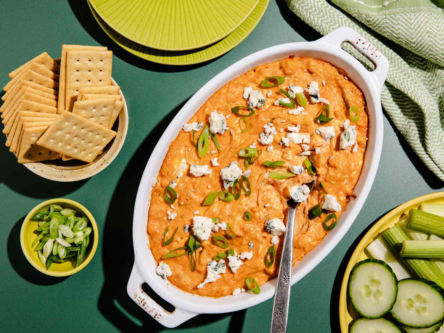 A white casserole dish filled with chicken dip next to a bowl filled with crackers.