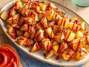 Angled view of a platter of patatas bravas topped with sauce and parsley all on a wooden table top