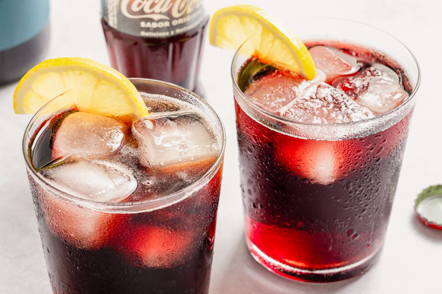 Two glasses of Kalimotxo with lemon wedges placed on the rims