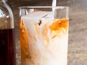 Milk being poured into a glass of iced chai