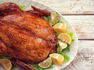 A roasted turkey on a white serving platter, garnished with lemon wedges and lettuce leaves