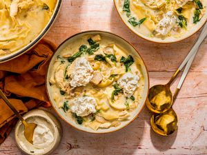 White chicken lasagna soup served in two bowls at a table setting with the spoons, napkins, and the rest of the soup in a dutch oven