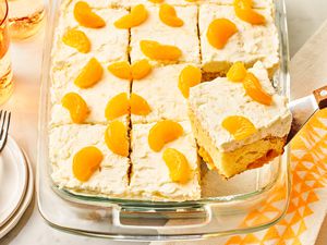 Angled view of a baking dish of pineapple and mandarin orange cake with a slice being removed with a spatula