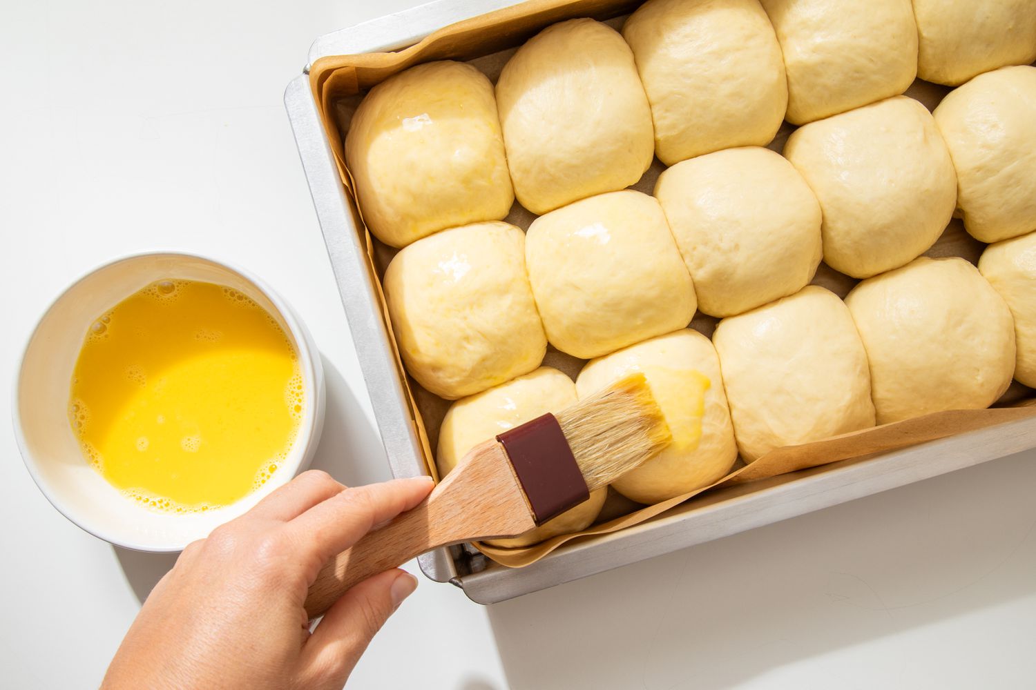 Egg washed brunshed onto the salted honey rolls in a baking pan using a pastry brush
