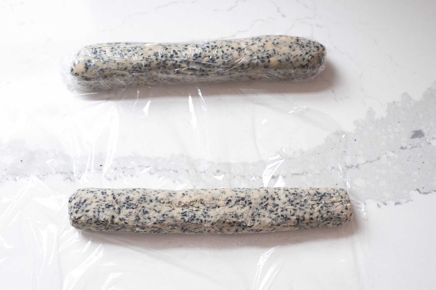 Thin and crispy sesame cookie dough shaped into two logs and wrapped in plastic wrap.