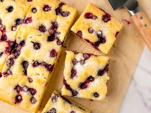 Sliced blueberry sheet cake with a serving spatula on parchment paper