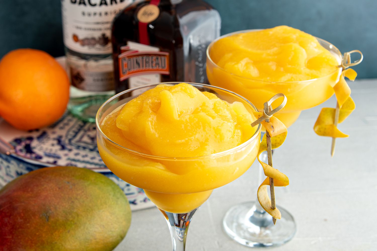 Frozen mango daiquiris in martini glasses garnished with curled mango peel.