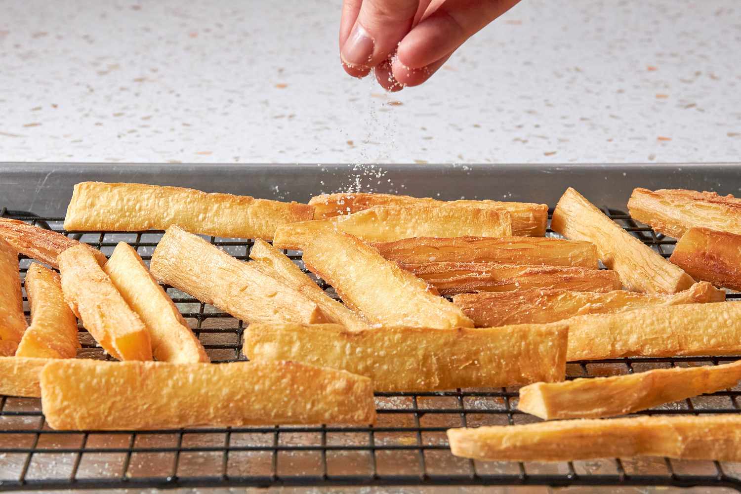 Salt Sprinkled Onto Yuca Fries Cooling on a Cooling Rack on a Baking Pan