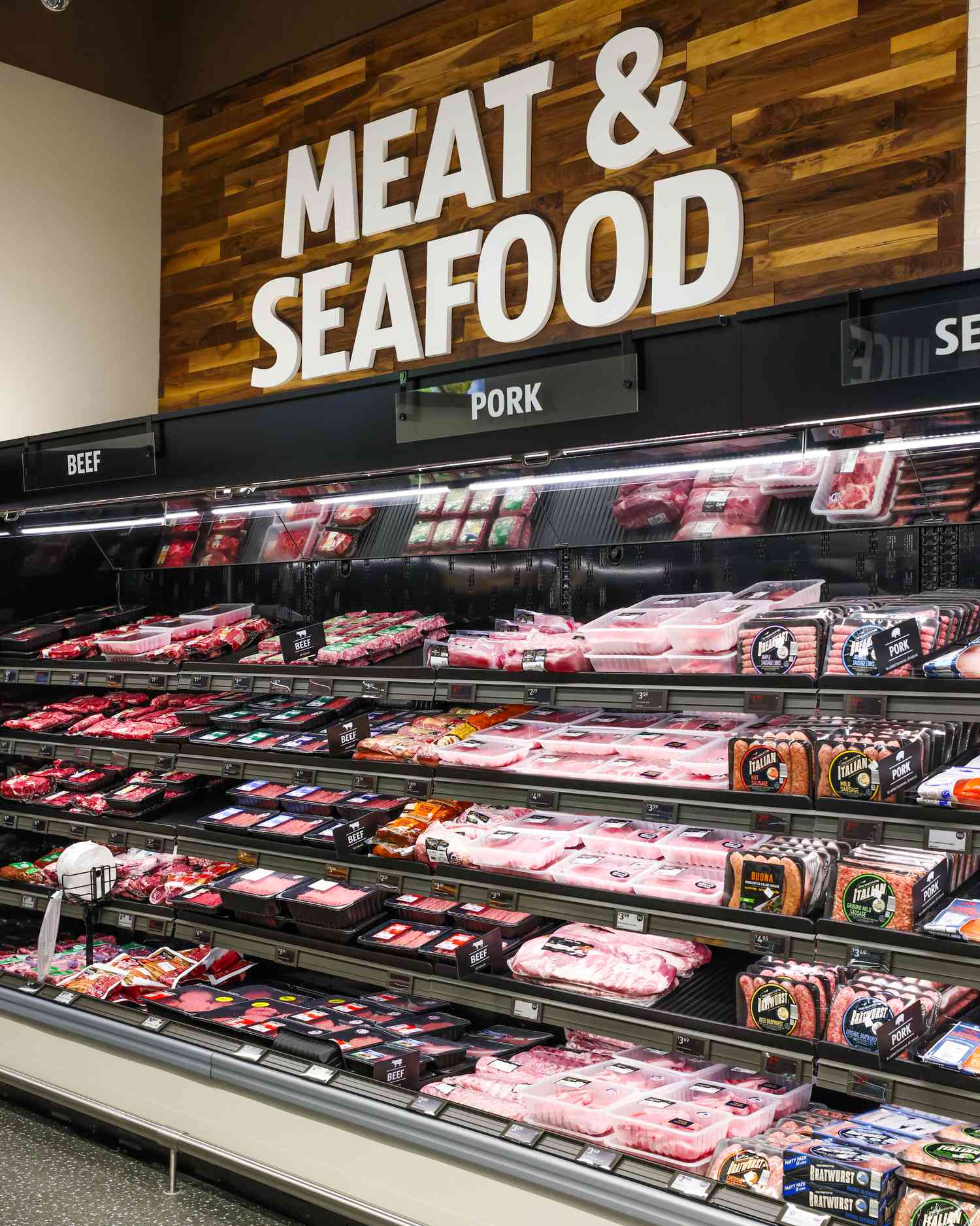 Supermarket meat and seafood section display, with packaged items organized on shelves under wooden signage