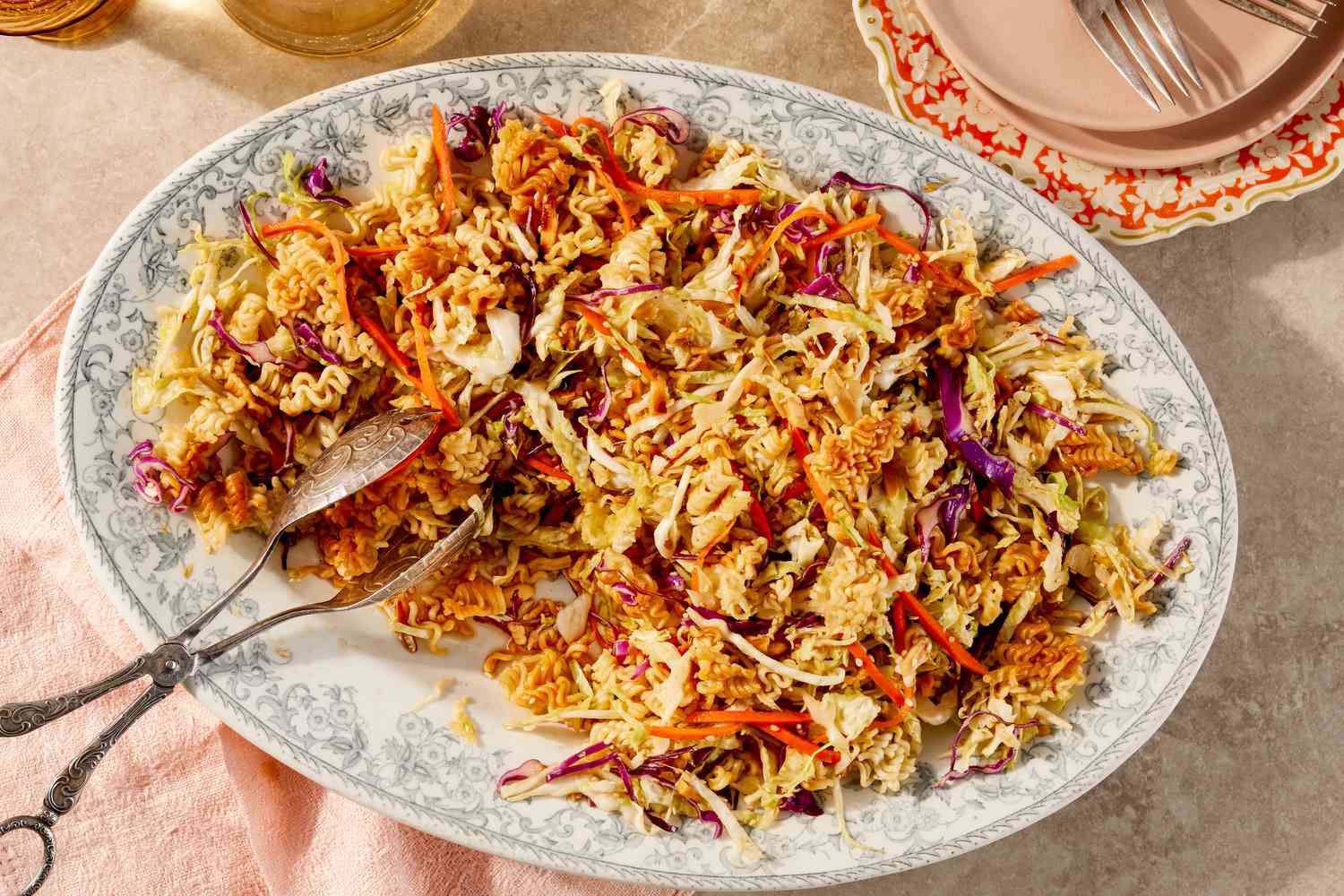 Overhead view of a decorative serving platter of crunchy ramen salad with serving scoops