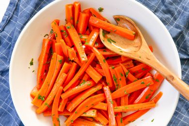 Overhead shot of a white shallow bowl with julienned carrots tossed in herbs and a wooden serving spoon