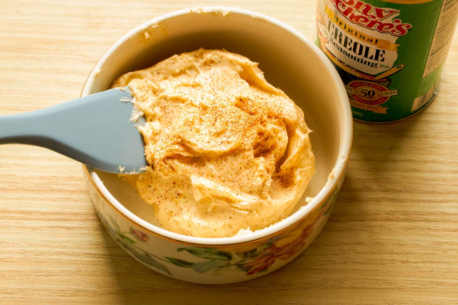 A bowl of seasoned butter with a spatula beside a can of Creole seasoning