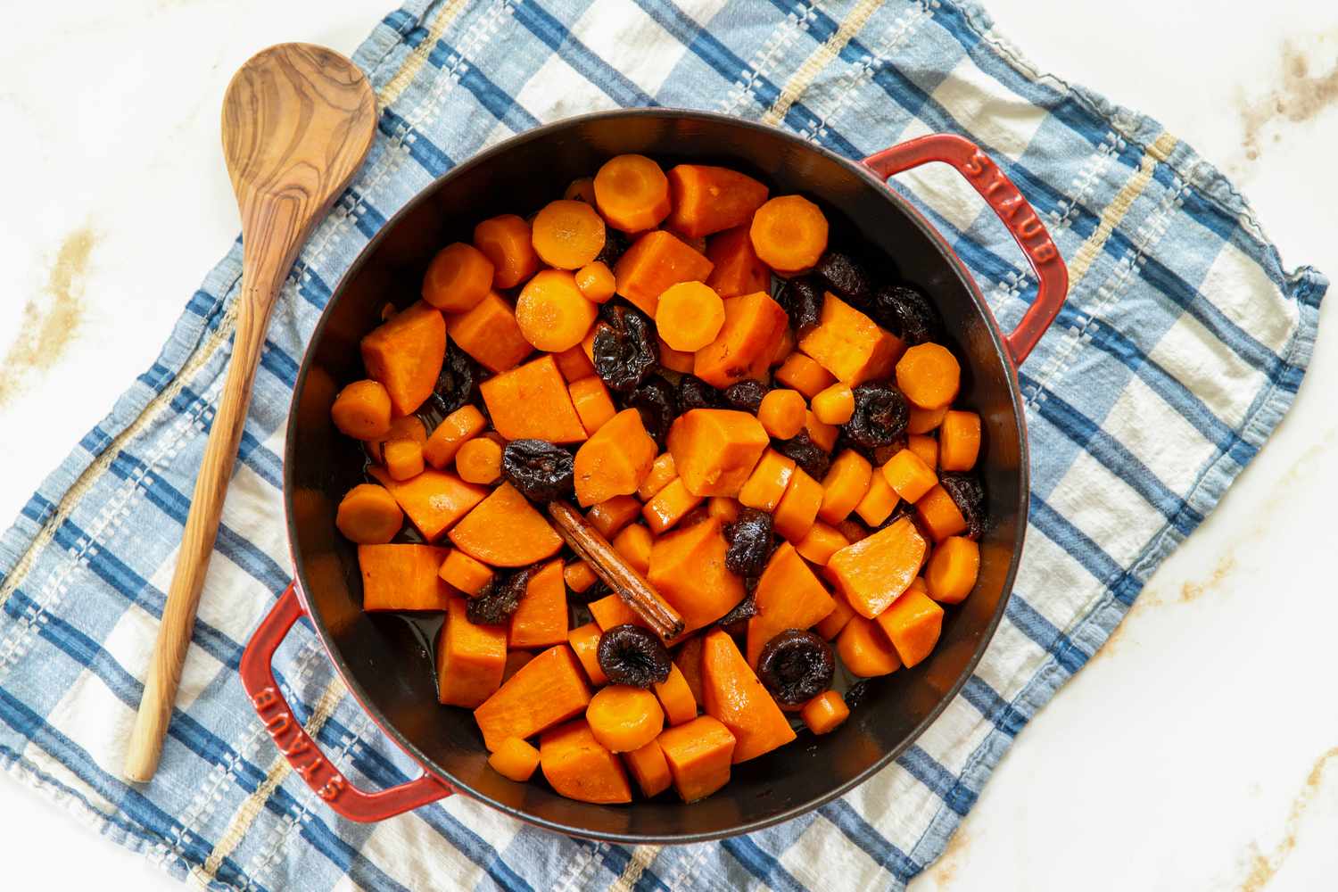 overhead view of Carrot and Sweet Potato Tzimmes in a roasting pan with a wooden spoon