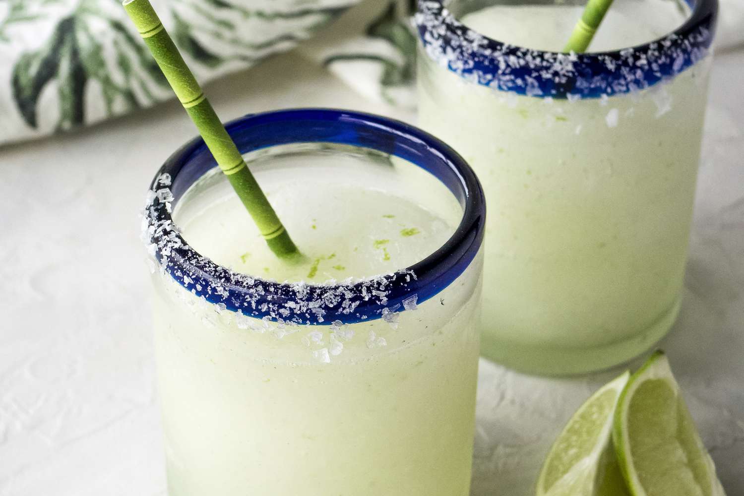 Frozen margarita recipe in two blue rimmed glasses with straws.