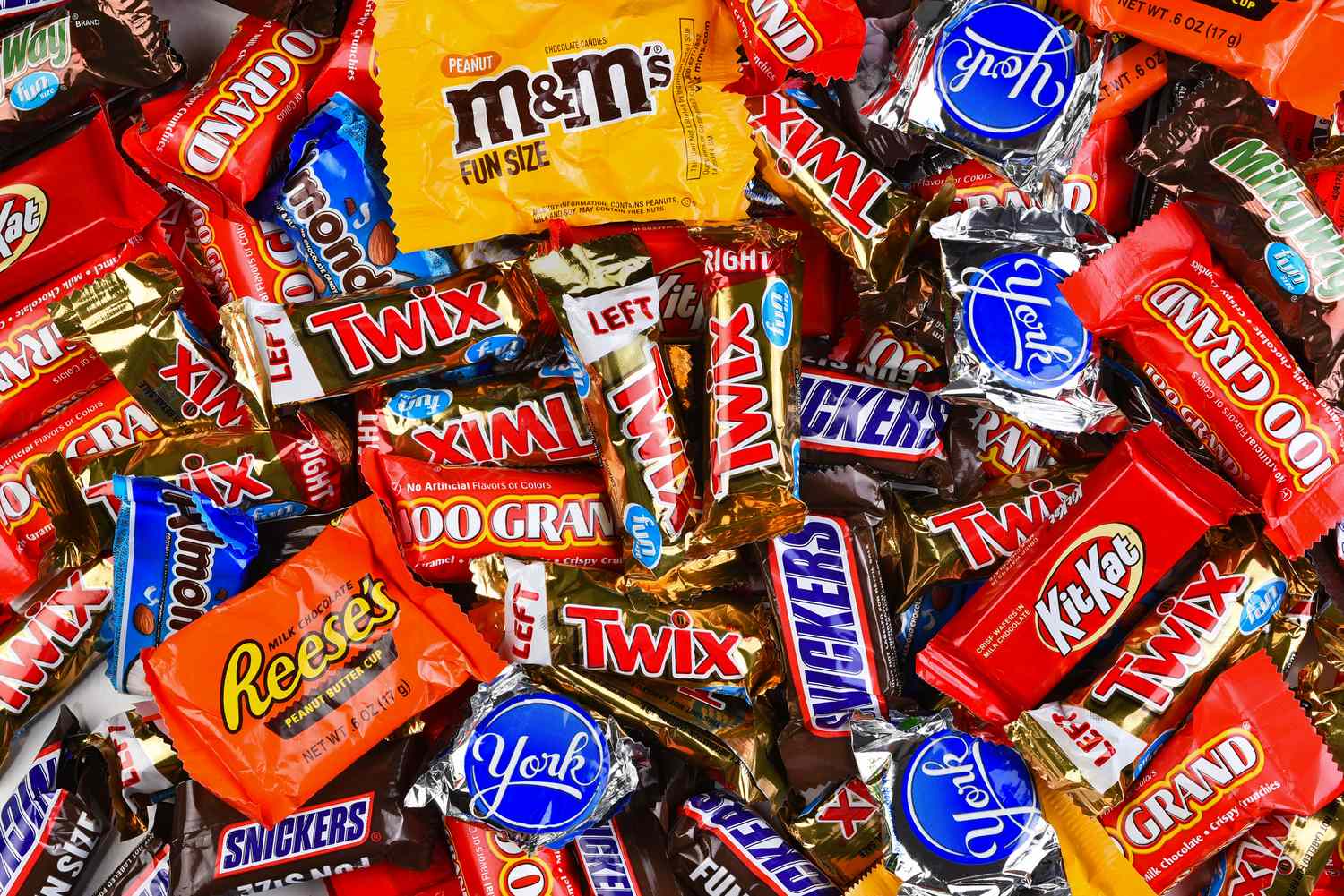 Assorted candies in wrappers including Snickers Twix Reeses and KitKat arranged in a pile