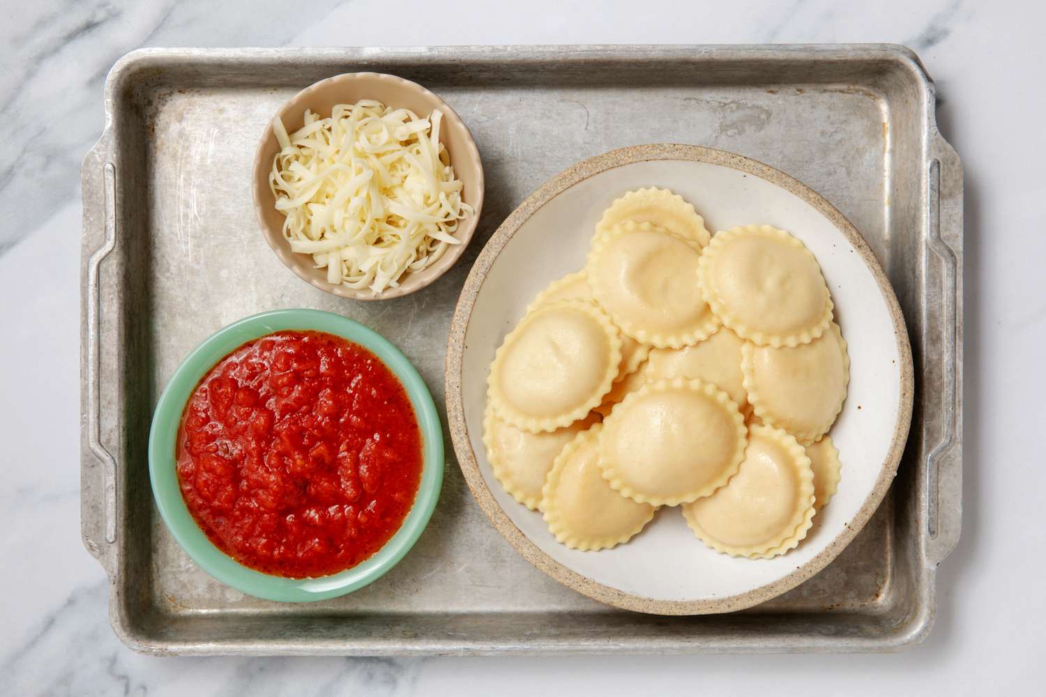 Tray with ravioli on a plate, a bowl of tomato sauce, and grated cheese